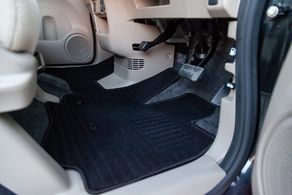 Clean car floor mats of black carpet under front driver seat in the workshop for the detailing vehicle before dry cleaning. Auto service industry. Interior of sedan.