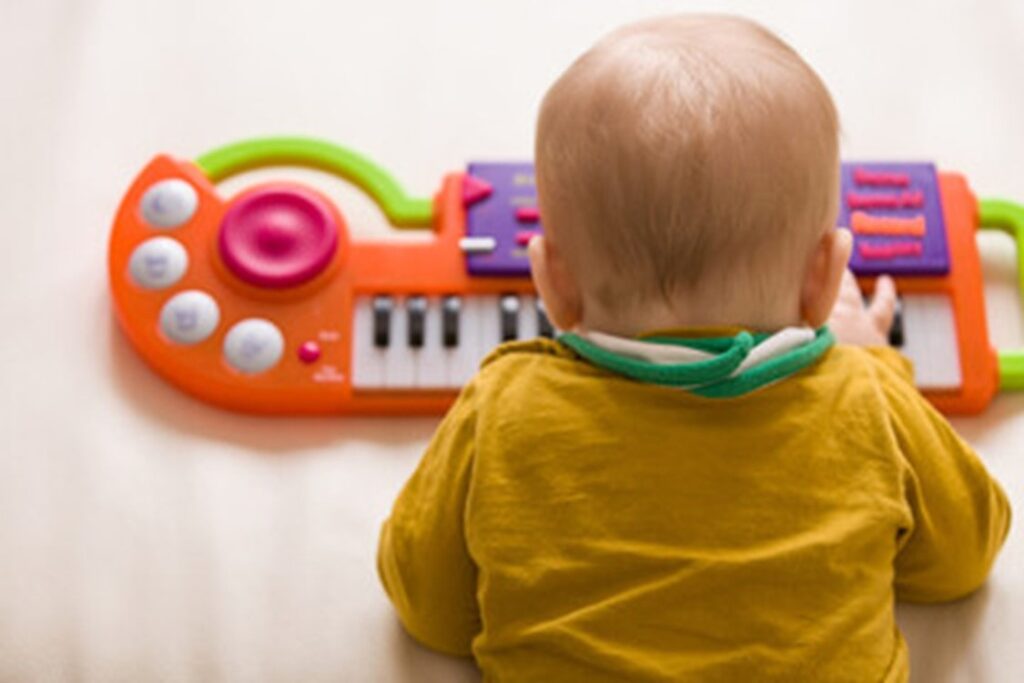 Top view on small cute baby boy sitting on the sofa and playing on the toy piano. A little boy learning to play piano listening to music. Early development for toddler. Musical education for kids