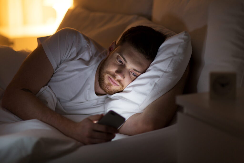 homem deitado na cama mexendo no celular